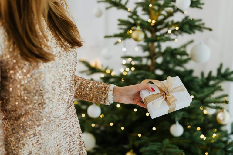 Femme qui porte un cadeaux de noël à coté du sapin.